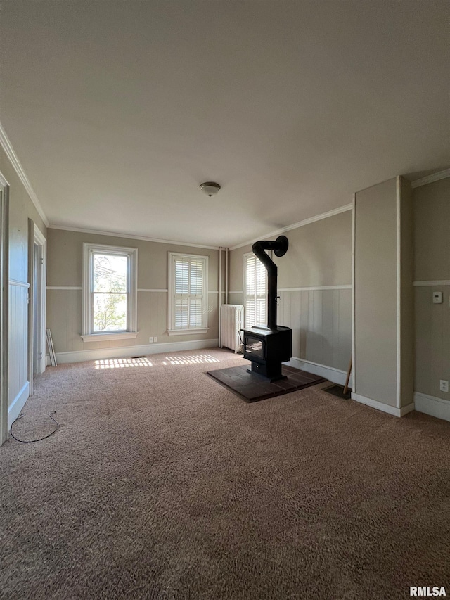 unfurnished living room with crown molding, a wood stove, radiator heating unit, and carpet floors