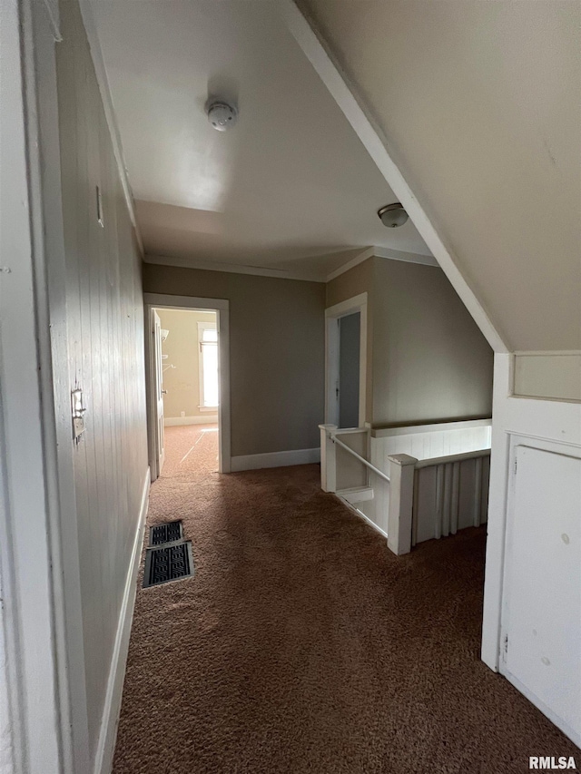 corridor with dark carpet, ornamental molding, and vaulted ceiling