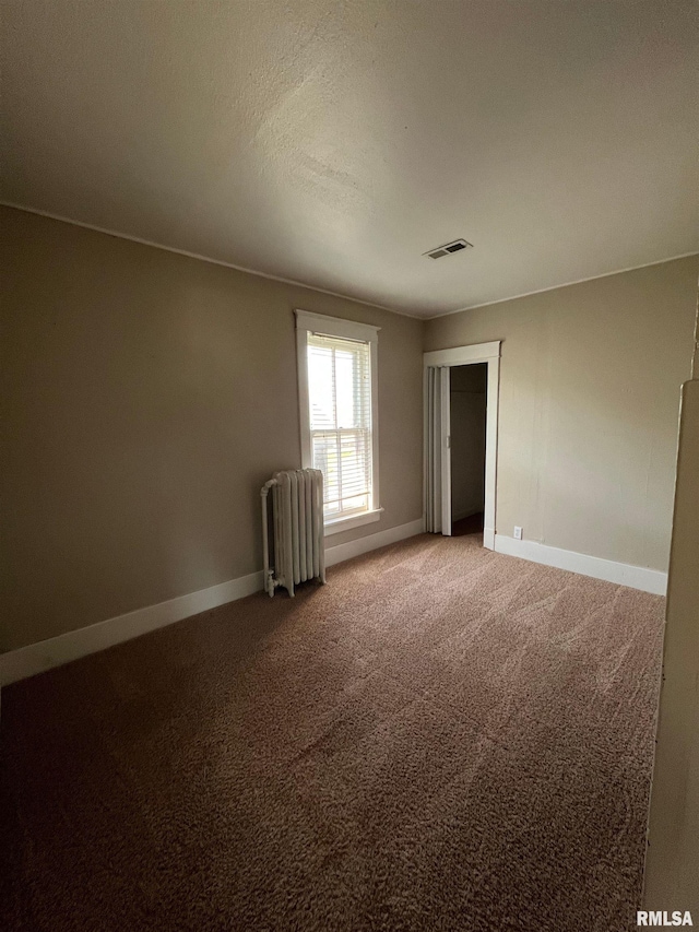 carpeted empty room featuring radiator heating unit