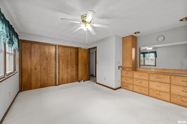 unfurnished bedroom with multiple closets, ceiling fan, and light colored carpet