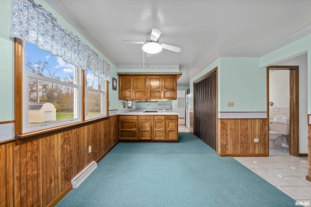 kitchen with ceiling fan, light colored carpet, and wooden walls