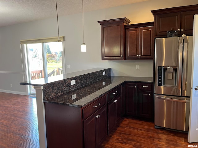 kitchen featuring dark hardwood / wood-style flooring, kitchen peninsula, stainless steel fridge, dark stone countertops, and decorative light fixtures