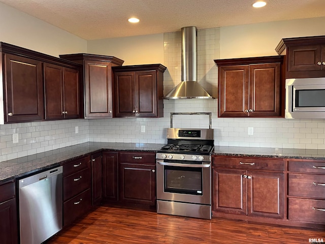 kitchen featuring appliances with stainless steel finishes, backsplash, dark stone countertops, and wall chimney range hood