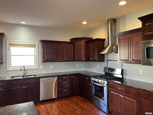 kitchen featuring wall chimney range hood, sink, dark hardwood / wood-style floors, decorative backsplash, and appliances with stainless steel finishes