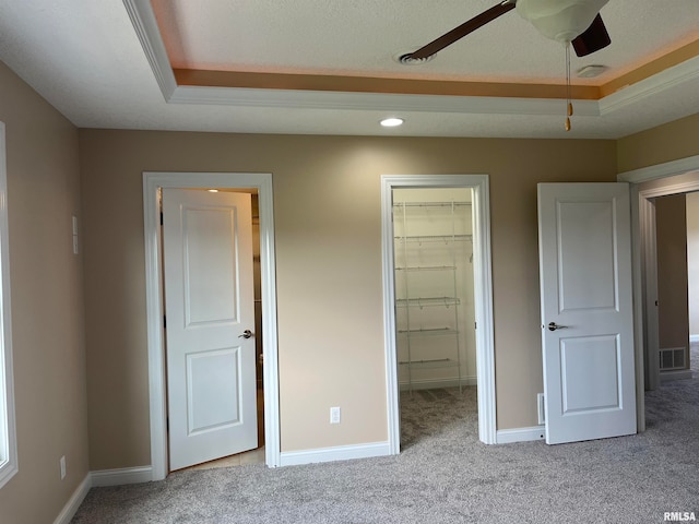 unfurnished bedroom featuring light colored carpet, a raised ceiling, ceiling fan, a spacious closet, and a closet