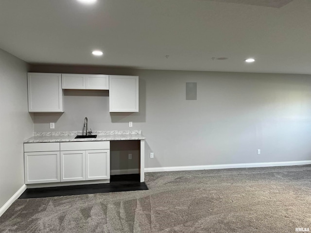 kitchen with light stone counters, sink, white cabinets, and dark carpet