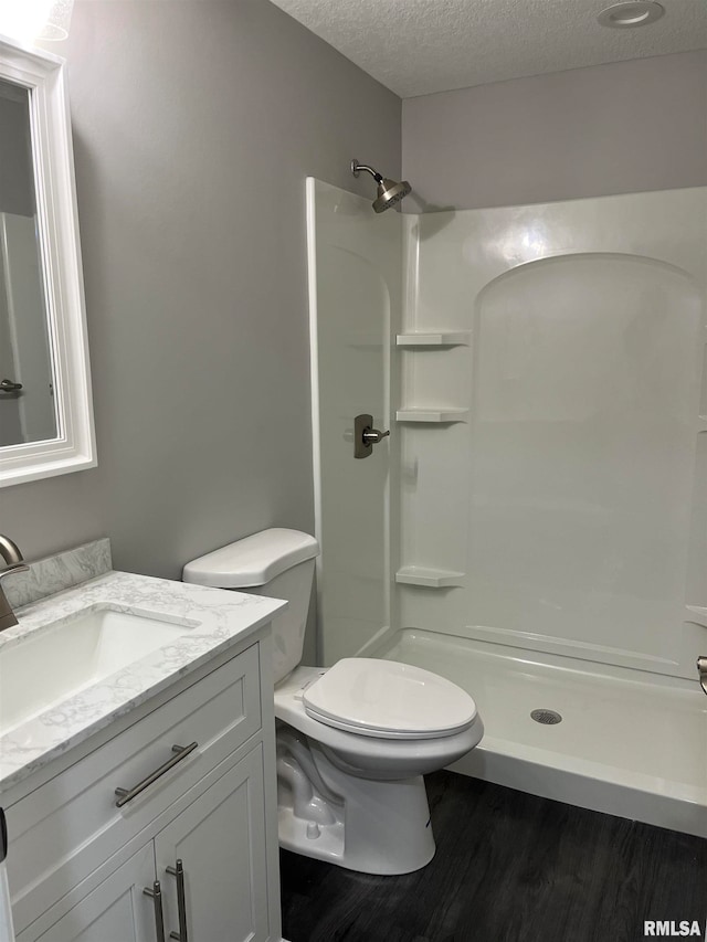 bathroom featuring walk in shower, wood-type flooring, a textured ceiling, toilet, and vanity