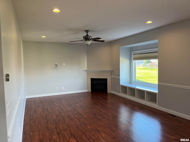 unfurnished living room with a tiled fireplace, ceiling fan, and dark hardwood / wood-style floors