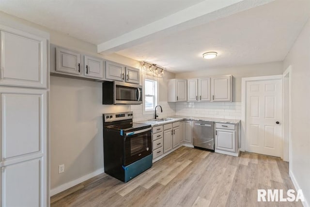 kitchen featuring appliances with stainless steel finishes, tasteful backsplash, gray cabinetry, sink, and light hardwood / wood-style flooring