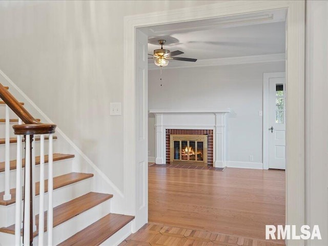 staircase with ceiling fan, hardwood / wood-style floors, ornamental molding, and a brick fireplace