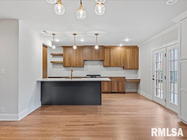 kitchen with kitchen peninsula, ornamental molding, sink, decorative light fixtures, and light hardwood / wood-style flooring