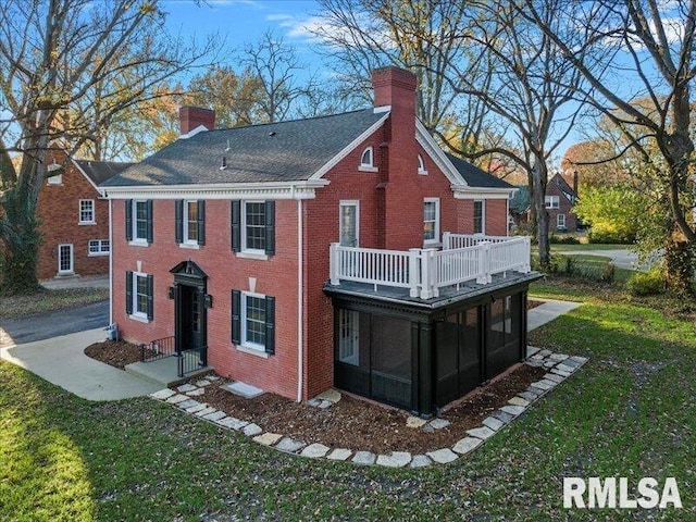 back of house with brick siding, a lawn, a chimney, and a sunroom