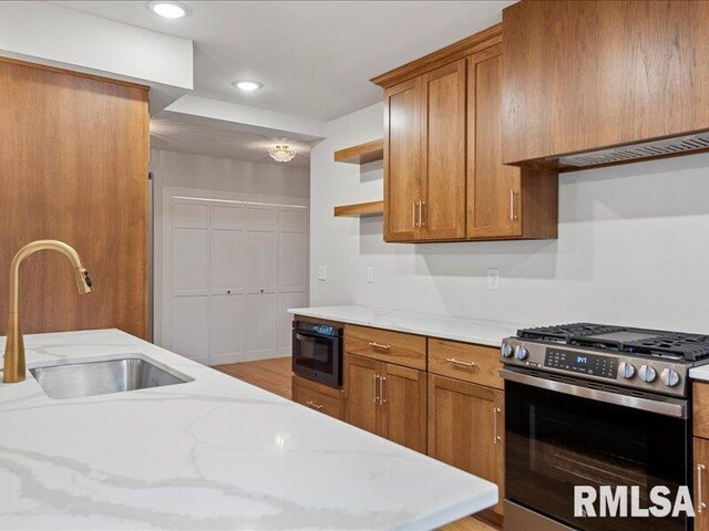 kitchen with open shelves, brown cabinetry, stainless steel gas stove, a sink, and light stone countertops