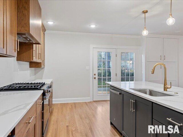 kitchen with stainless steel appliances, light stone counters, a sink, and decorative light fixtures