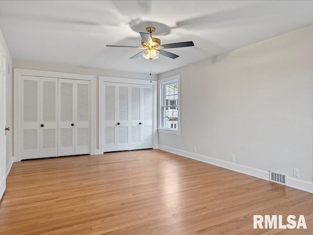 unfurnished bedroom with ceiling fan, light hardwood / wood-style flooring, and multiple closets