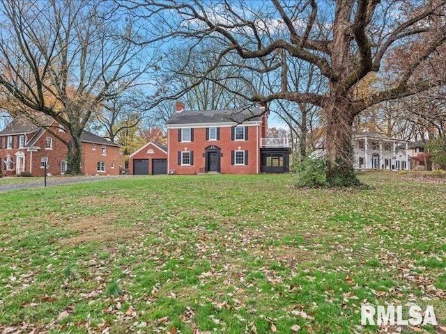 view of front of house with a front lawn, a chimney, a detached garage, and brick siding