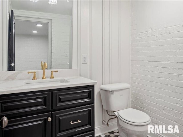 bathroom with vanity, toilet, and brick wall