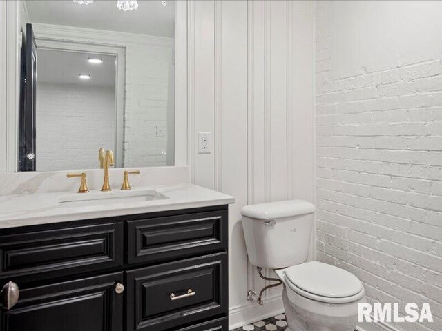 half bath with brick wall, vanity, and toilet