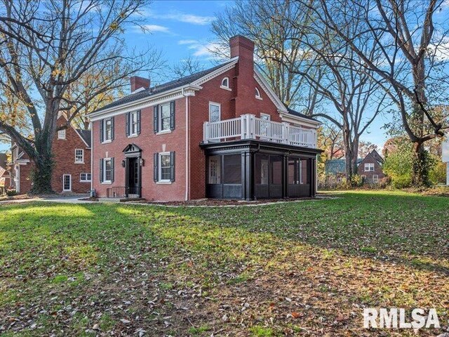 view of front of property with brick siding, a chimney, a front yard, and a sunroom