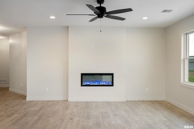 unfurnished living room featuring a glass covered fireplace, plenty of natural light, light wood-style flooring, and visible vents