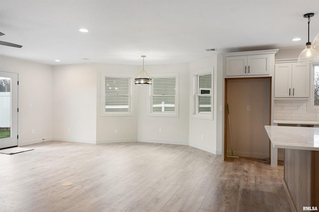 interior space featuring backsplash, light wood-type flooring, white cabinetry, and hanging light fixtures