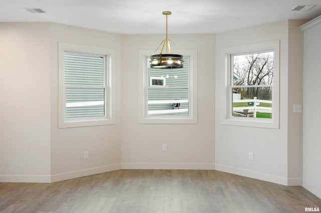unfurnished dining area featuring baseboards, light wood finished floors, a chandelier, and visible vents