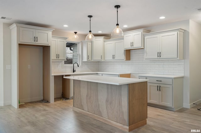 kitchen featuring hanging light fixtures, light hardwood / wood-style floors, tasteful backsplash, a kitchen island, and white cabinetry