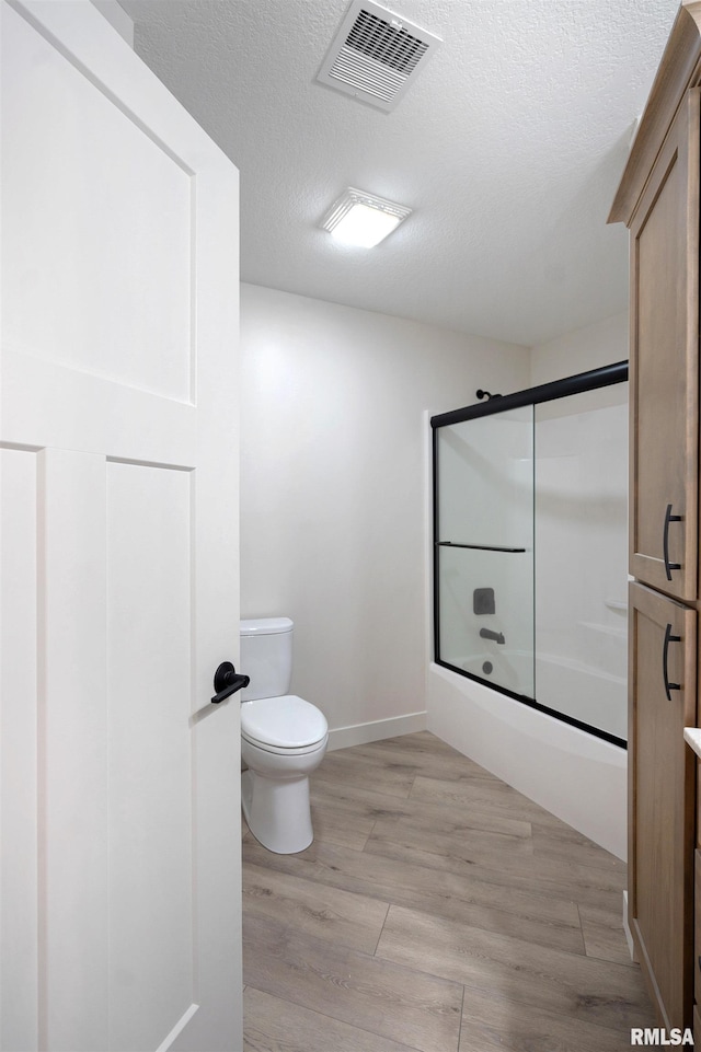 bathroom with a textured ceiling, visible vents, wood finished floors, bath / shower combo with glass door, and toilet