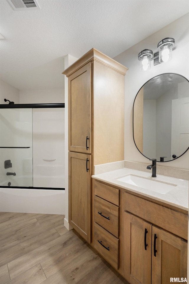 bathroom with a textured ceiling, visible vents, wood finished floors, vanity, and enclosed tub / shower combo