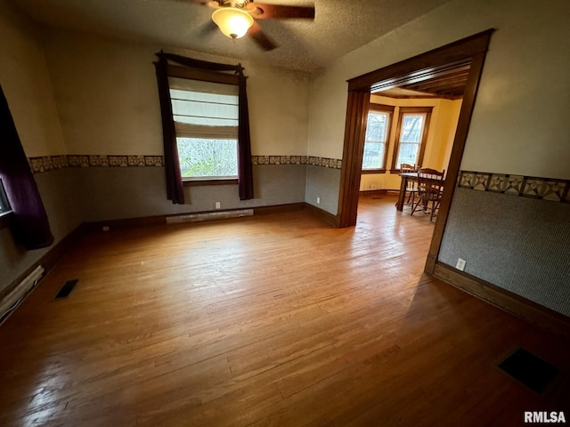 empty room featuring ceiling fan, light wood-type flooring, a textured ceiling, and baseboard heating