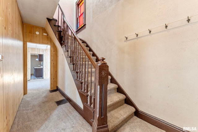 staircase with carpet flooring and wood walls