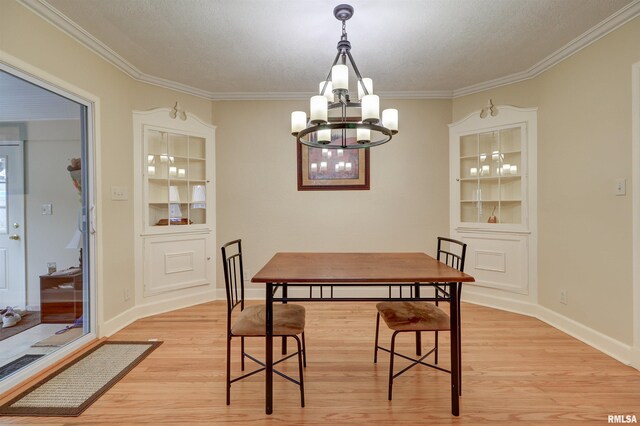 dining space with crown molding, light hardwood / wood-style floors, built in features, and a notable chandelier