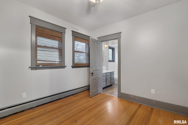 unfurnished bedroom featuring light wood-type flooring, ceiling fan, a baseboard heating unit, and connected bathroom