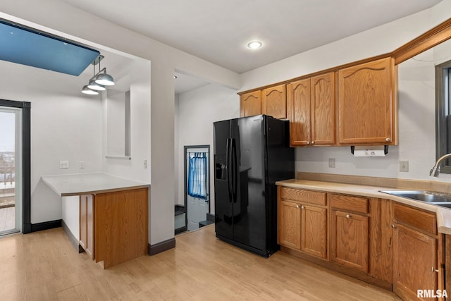 kitchen featuring black fridge with ice dispenser, light hardwood / wood-style floors, pendant lighting, and sink