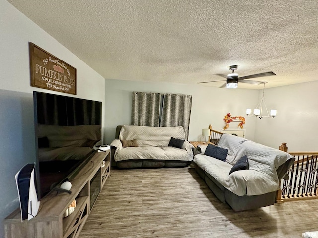 living room featuring ceiling fan with notable chandelier, hardwood / wood-style floors, and a textured ceiling