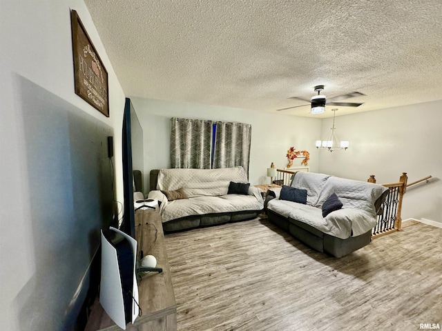 living room featuring ceiling fan with notable chandelier, wood-type flooring, and a textured ceiling