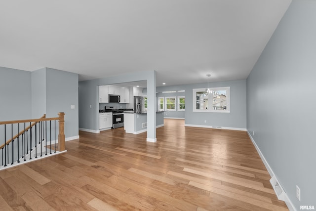 unfurnished living room featuring a chandelier and light wood-type flooring