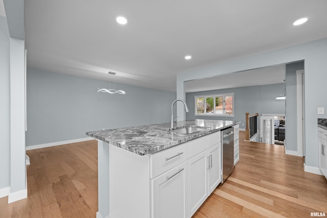 kitchen with white cabinets, dishwasher, sink, light stone counters, and a center island with sink