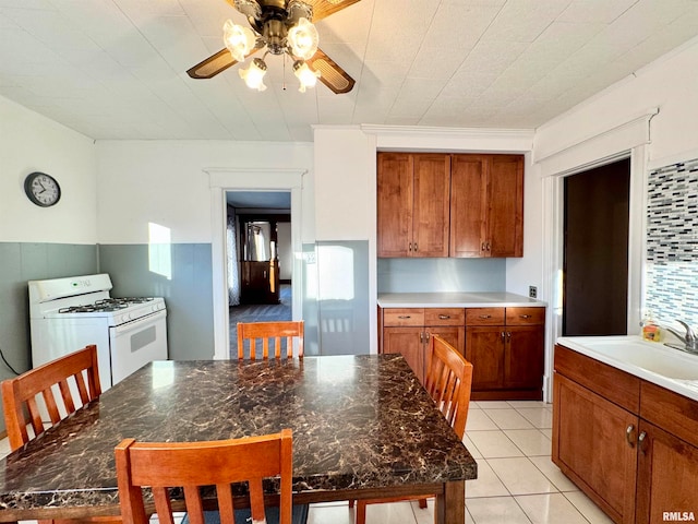 kitchen with light tile patterned floors, white range with gas cooktop, brown cabinetry, and a sink