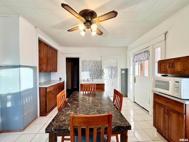 kitchen with ceiling fan, white microwave, light tile patterned flooring, a sink, and brown cabinetry