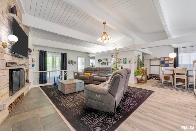 living room featuring a stone fireplace, hardwood / wood-style floors, lofted ceiling with beams, and an inviting chandelier