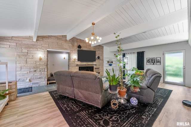 living room with hardwood / wood-style floors, vaulted ceiling with beams, a stone fireplace, and an inviting chandelier