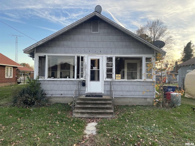 bungalow-style home with entry steps, a front lawn, and a sunroom