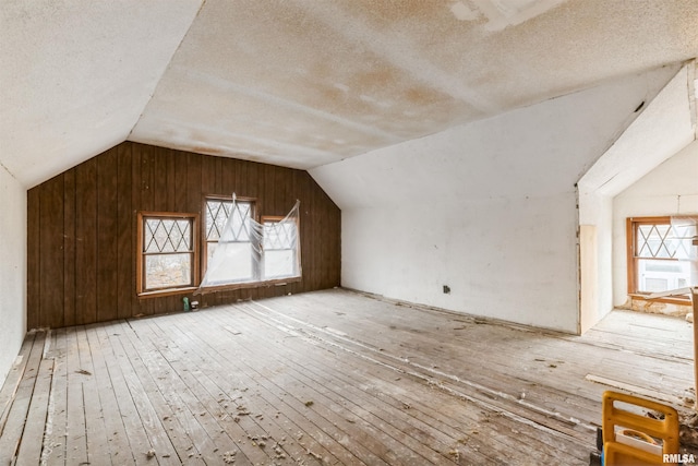 additional living space featuring vaulted ceiling, wooden walls, light hardwood / wood-style flooring, and a textured ceiling