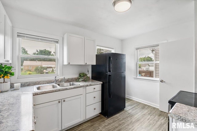 kitchen with light hardwood / wood-style floors, black refrigerator, white cabinetry, and sink