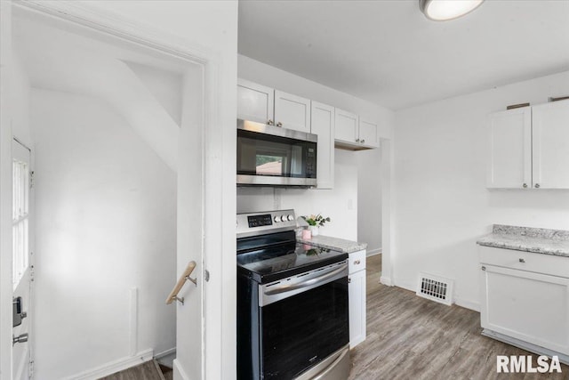 kitchen featuring white cabinets, light stone countertops, appliances with stainless steel finishes, and light hardwood / wood-style flooring