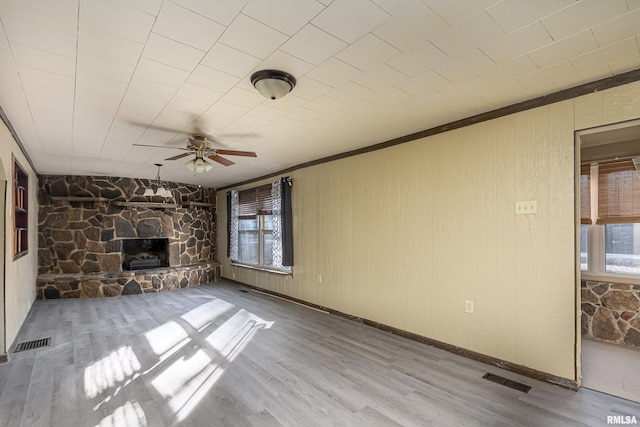 unfurnished living room featuring hardwood / wood-style flooring, ceiling fan, ornamental molding, and a stone fireplace