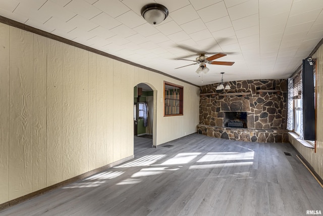 unfurnished living room featuring ornamental molding, wooden walls, ceiling fan, a fireplace, and hardwood / wood-style floors