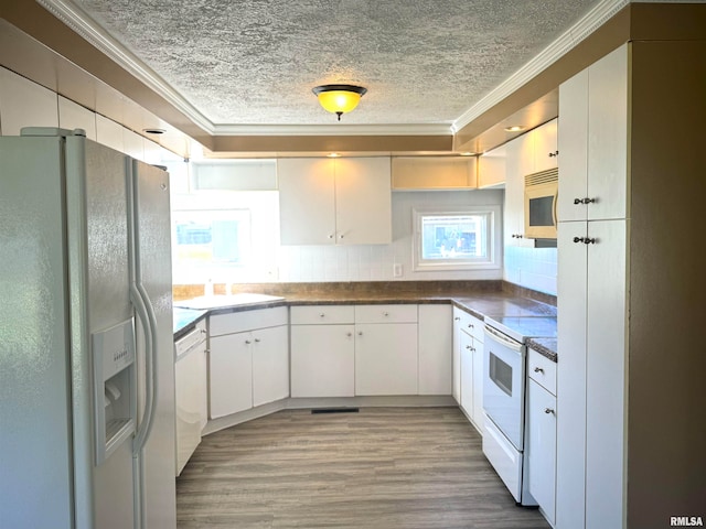 kitchen featuring white appliances, a sink, ornamental molding, white cabinetry, and dark countertops