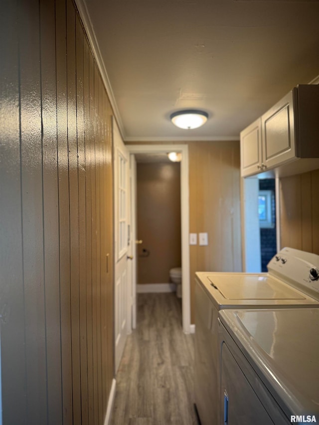 clothes washing area with washing machine and clothes dryer, wood walls, and wood-type flooring